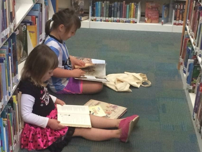 Children reading books on library floor.