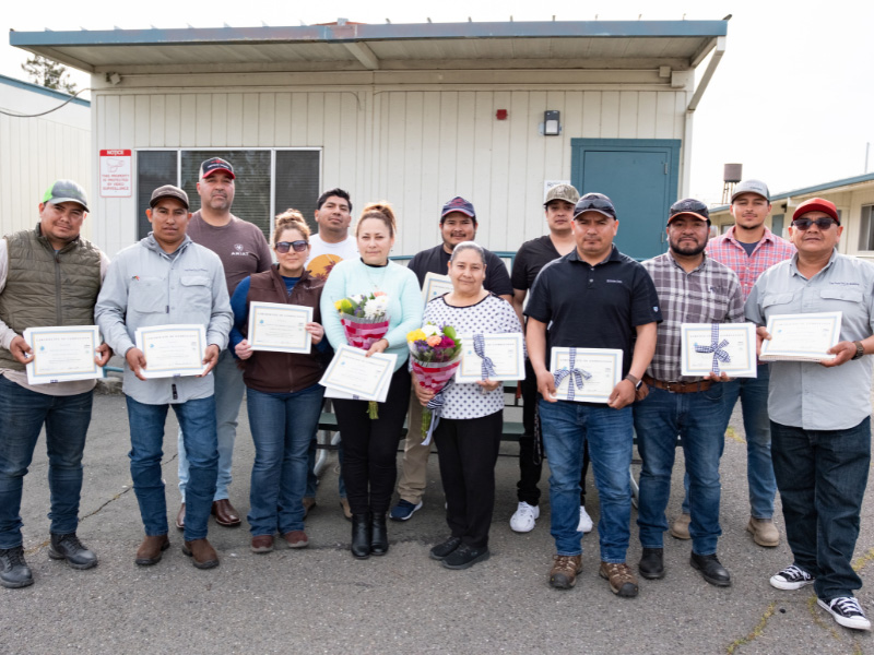 Group holding certificates and flowers outside building.