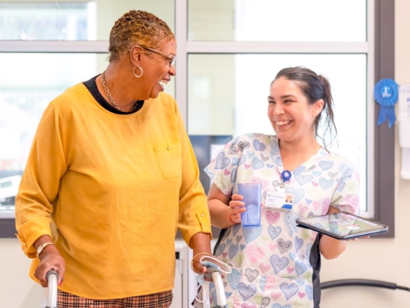 Smiling nurse assisting elderly woman with walker.