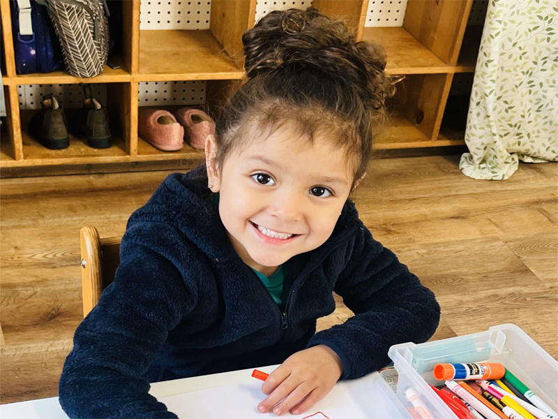 Child drawing with markers smiling at table.