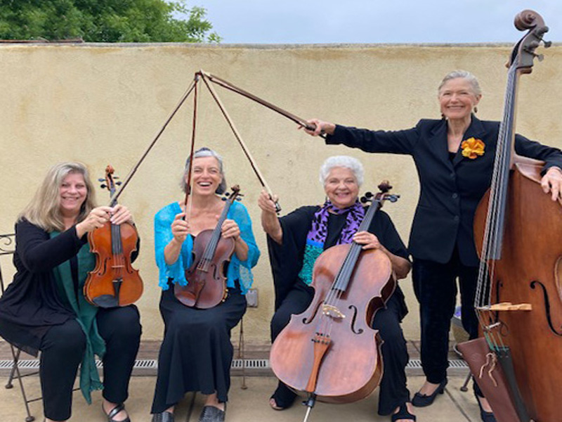 Four women musicians with string instruments, smiling.