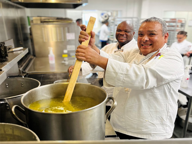 Chefs stirring large pot in kitchen